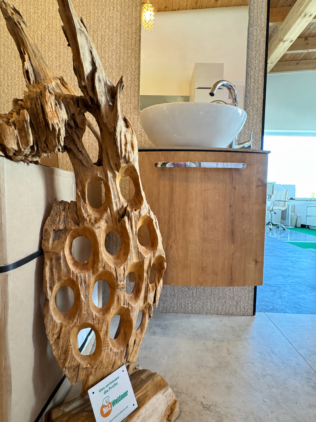 Holzskulptur mit runden Öffnungen vor einem Waschplatz mit Holzunterschrank